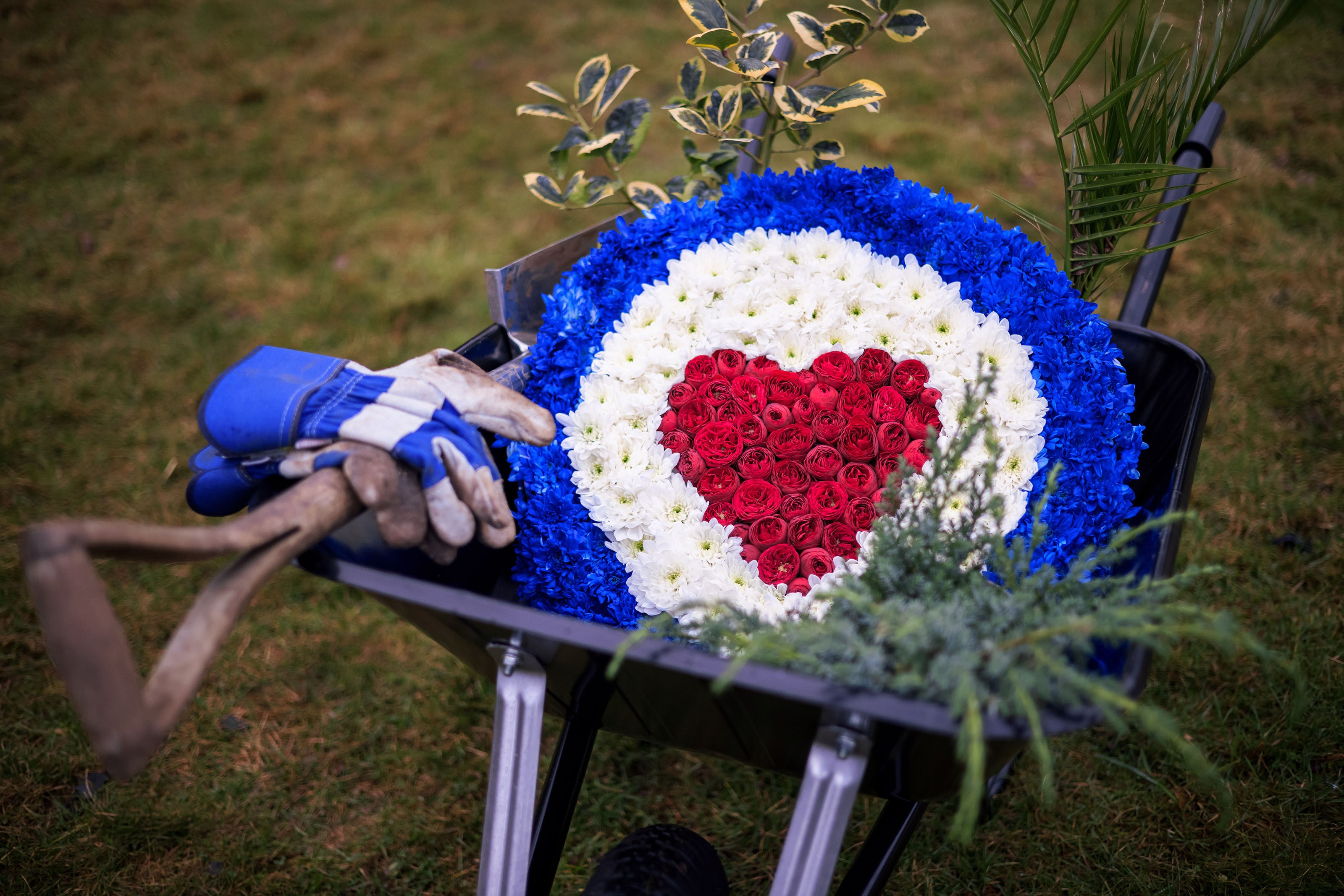Wheelbarrow with RAF Roundel flower wreath, spade, and plants.